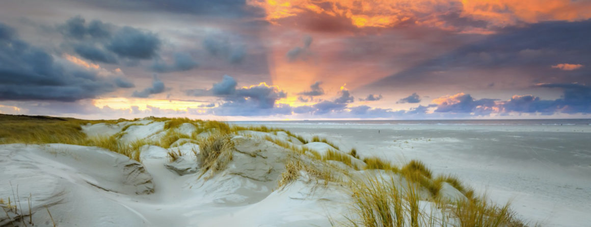 Zon en wolken boven zee en duinen met helmgras